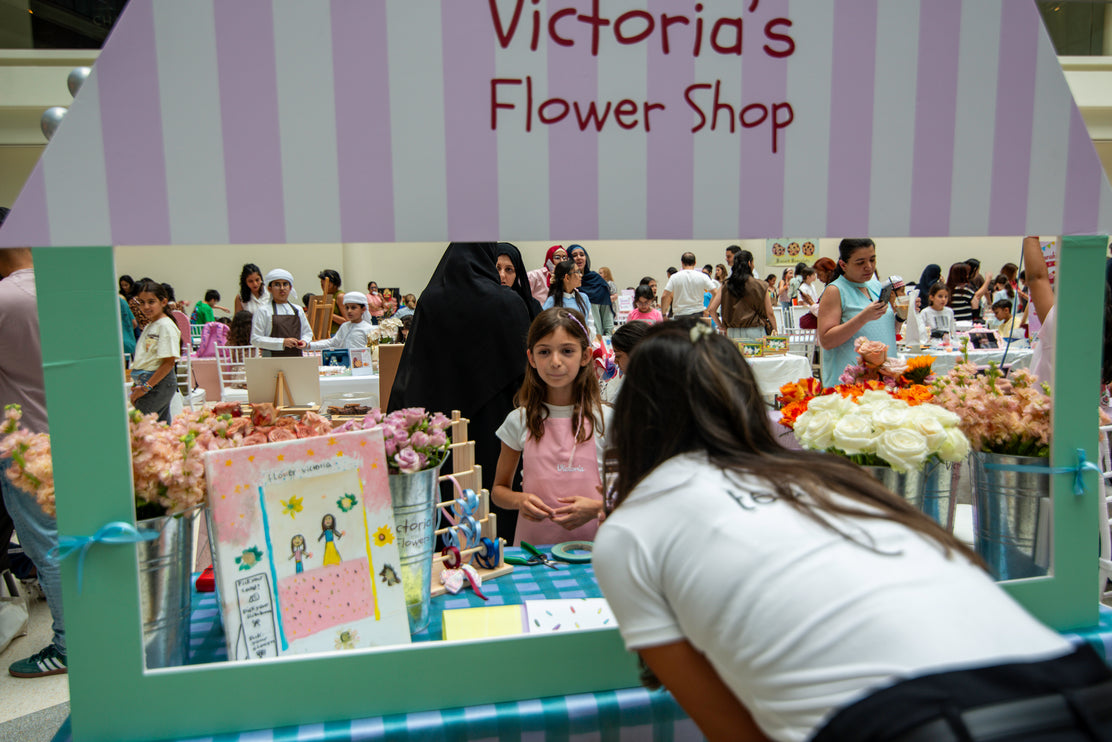 Children's flower shop booth at an event with 'Victoria's Flower Shop' sign.